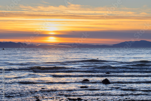 Beautiful morning seascape. Sunrise over the sea and mountains. Sun in the clouds. View from the shore to the sea. Sea of Okhotsk  Magadan region  Far East of Russia.