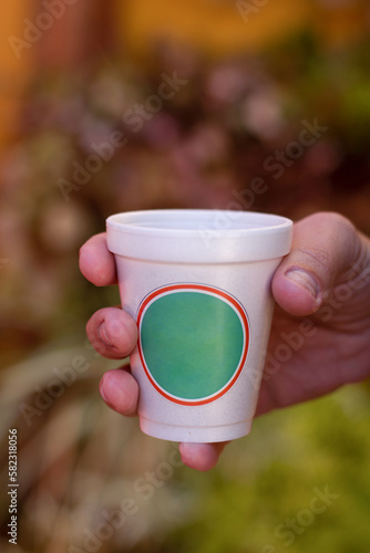 mano sostiene un vaso de telgopor blanco con etiqueta redonda verde contorno rojo photo