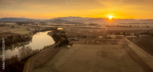 Aerial Panoramic View of the Skagit River and Surrounding Farmlands. Sunrise over the Cascade Mountains in the Pacific Northwest bathes the scenic Skagit Valley, Washington, in beautiful warm light.