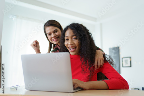 Caucasian white and African black ethnic women using laptop - notebook computer and having a discussion together in the room. Young woman colleagues working together on laptop computer. © DG PhotoStock