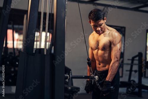 Asian man athletic weight training triceps muscles workout in fitness gym. Weight training exercise in concept of health and wellness. Bodybuilder shirtless workout at gym.