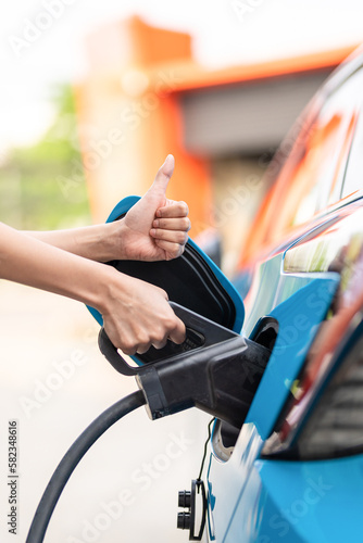 Woman plugging in the charger into a socket of her blue electric car at a charging station in the street © ND STOCK