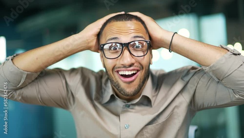 Webcam view. Close up of amazed happy businessman looking surprised at camera or laptop screen while sitting in office. Excited man in glasses saw pleasant content or read good news. Wow effect