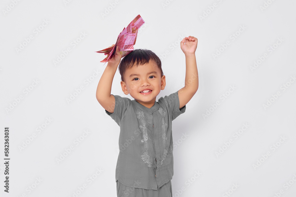 Excited toddler Asian muslim boy holding money banknotes and celebrating success isolated on white studio background Excited toddler Asian muslim boy holding money banknotes and celebrating success isolated on white studio background