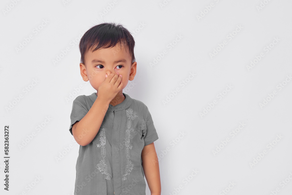 Disgusted Toddler Asian muslim boy feeling disgusted, holding her nose to avoid smelling foul isolated on white studio background Disgusted Toddler Asian muslim boy feeling disgusted, holding her nose to avoid smelling foul isolated on white studio background