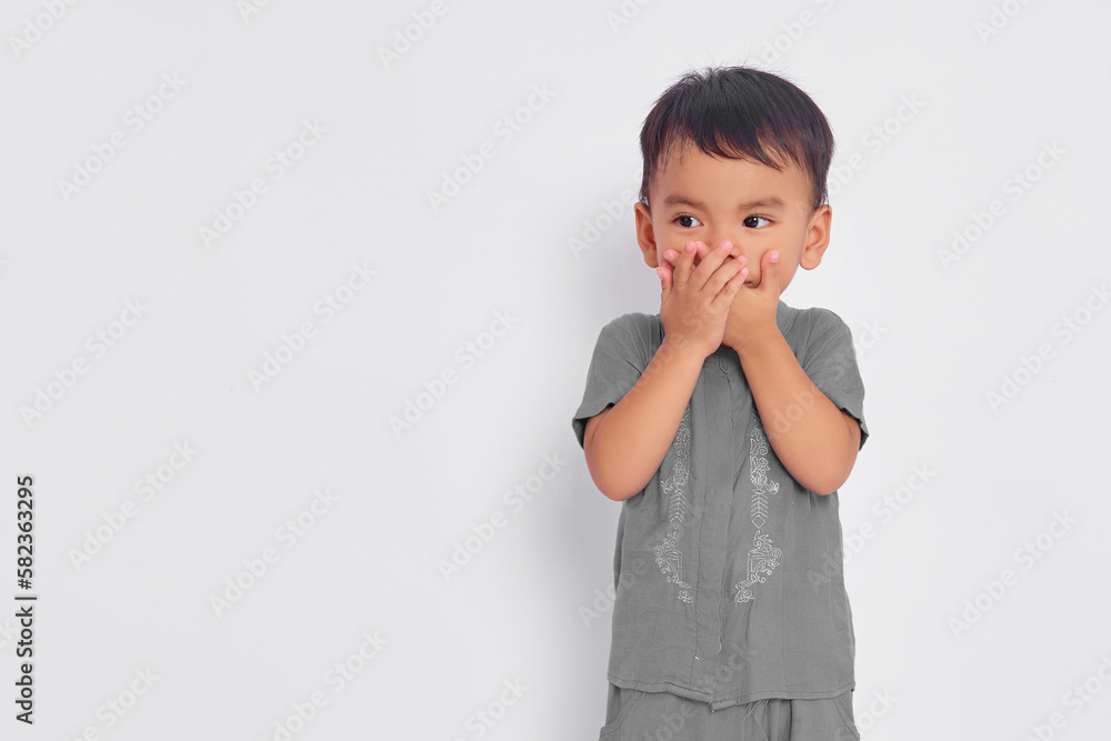 Shocked toddler Asian muslim boy covering mouth with hands and looking at empty space isolated on white studio background Shocked toddler Asian muslim boy covering mouth with hands and looking at empty space isolated on white studio background