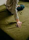 Hand of a woman sitting on a bed with green sheets