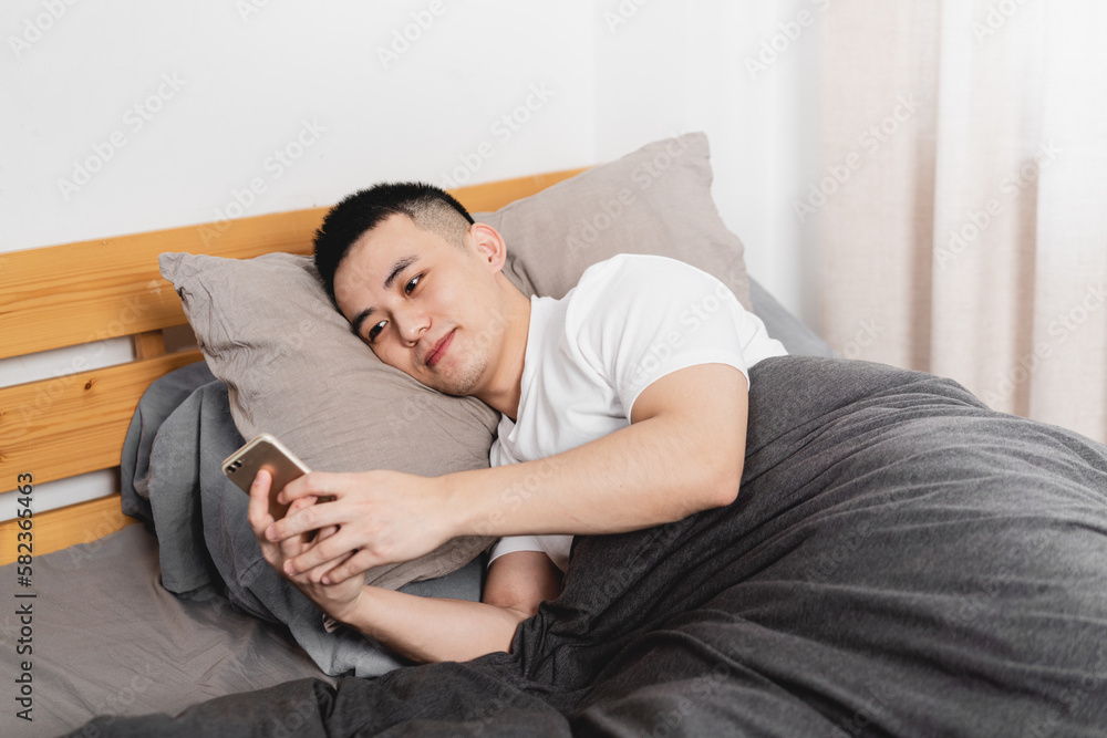 Asian man is lying in the bed using mobile phone.