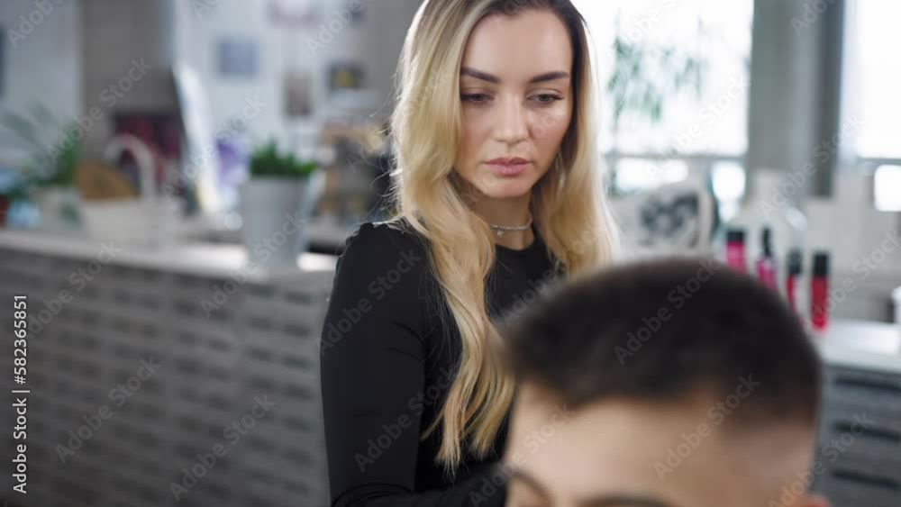 A young woman blonde hairdresser cuts a client's hair a man in a beauty salon. Camera movement A young woman blonde hairdresser cuts a client's hair a man in a beauty salon. Camera movement