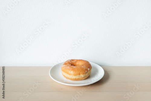 Sweet delicious glazed donut on white plate.
