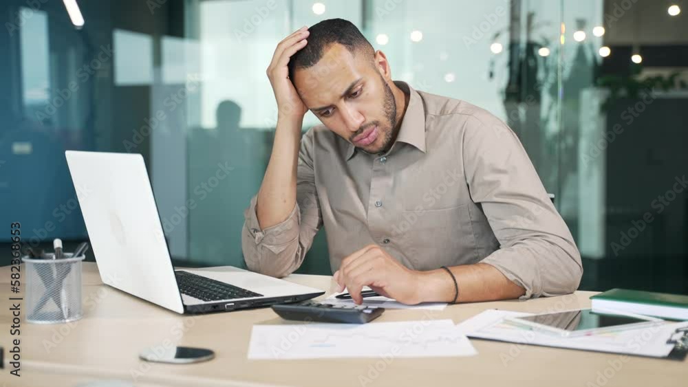 Exhausted young man bored at work using laptop while sitting at workplace at desk in modern office. Overworked mixed race worker is tired, feeling unwell. He cannot concentrate, he is in a bad mood Exhausted young man bored at work using laptop while sitting at workplace at desk in modern office. Overworked mixed race worker is tired, feeling unwell. He cannot concentrate, he is in a bad mood