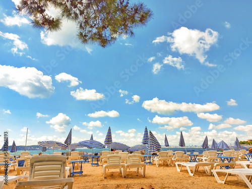 Sun loungers and umbrellas on a sandy beach in sunny weather and white clouds in the blue sky