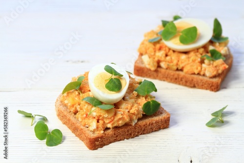 Egg salad over brown bread and cut egg on white table. Homemade spread made from eggs, vegetable and mayonnaise. Decorated healthy young buckwheat.