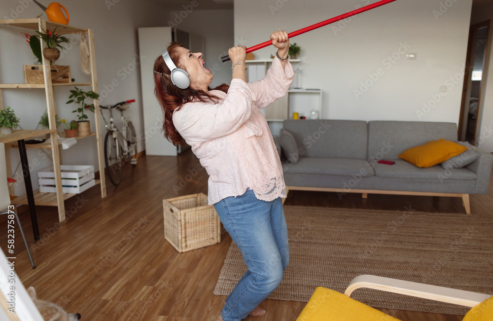 mature woman cleaning the house, she gets excited and uses the microphone broom while cleaning and listening to music with headphones