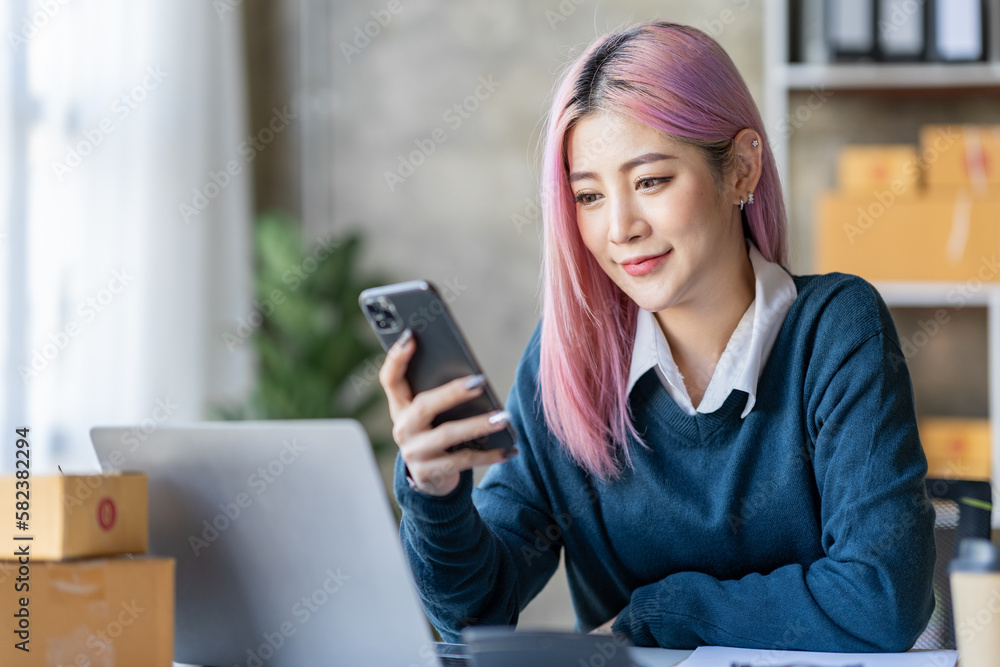 Portrait of a happy Asian businesswoman working on a laptop computer at her home office while using a mobile phone. Smiling businesswoman contacting the business to talk about online products. Portrait of a happy Asian businesswoman working on a laptop computer at her home office while using a mobile phone. Smiling businesswoman contacting the business to talk about online products.