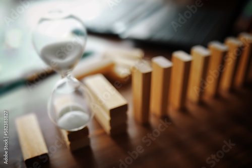 domino effect concept with wooden tiles blocked by hourglass with background