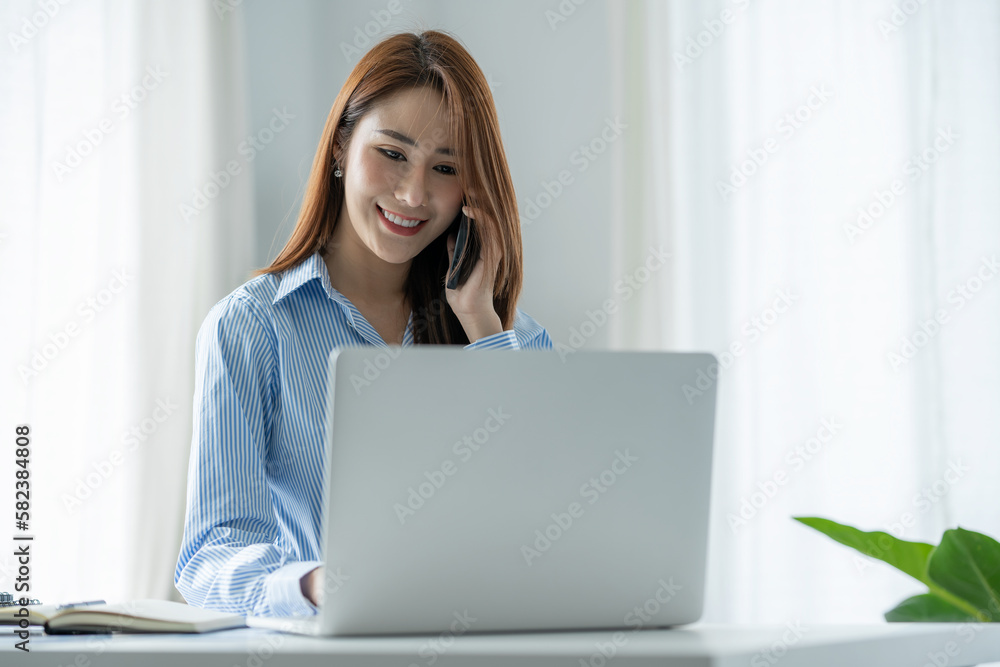 Attractive businesswoman using a smartphone for happy business discussion while working on a laptop at a modern office. Attractive businesswoman using a smartphone for happy business discussion while working on a laptop at a modern office.