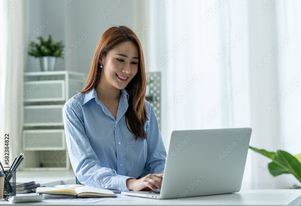 Beautiful Asian businesswoman sitting at work saving data Happy checking financial details on laptop computer in the office. Beautiful Asian businesswoman sitting at work saving data Happy checking financial details on laptop computer in the office.