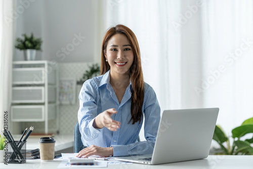 Pretty smiling Asian businesswoman sitting on camera relaxing on the desk after verifying financial documents Happy validation at the office. © crizzystudio