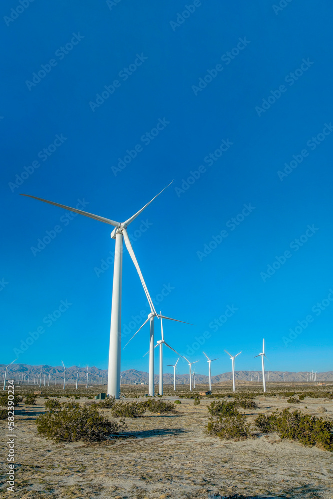Windmills on vast dry land with mountain and blue sky view in the background. The windpumps have three blades that produce renewable energy using wind power. Windmills on vast dry land with mountain and blue sky view in the background. The windpumps have three blades that produce renewable energy using wind power.