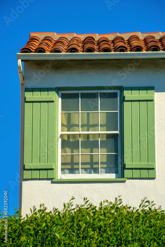 Hidden or secret window with green shutters adobe red roof tiles with front yard shrubs and clear blue sky copy space