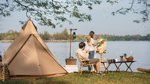 Camping concept, Young couple doing activity outside tent to painting on canvas and drinking coffee © Pichsakul