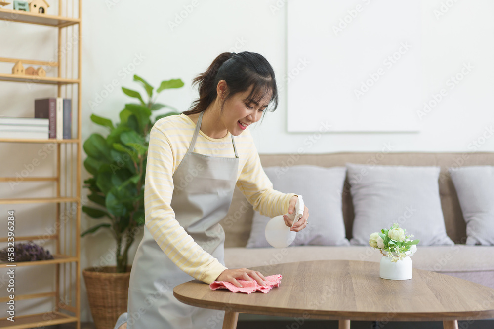 Maid spraying cleaner on wood table and wiping dirty with microfiber fabric to cleaning in home Maid spraying cleaner on wood table and wiping dirty with microfiber fabric to cleaning in home