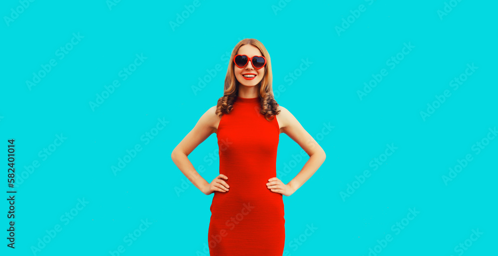Summer portrait of beautiful young woman posing wearing dress and red heart shaped sunglasses on blue background Summer portrait of beautiful young woman posing wearing dress and red heart shaped sunglasses on blue background