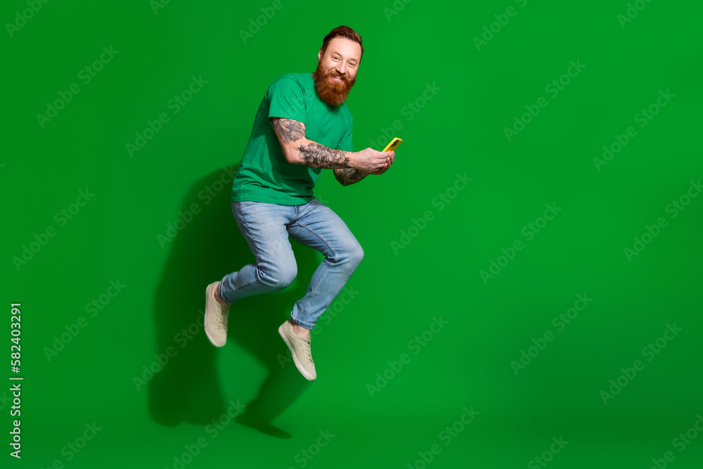 Full size profile portrait of excited energetic person jumping use smart phone empty space isolated on green color background Full size profile portrait of excited energetic person jumping use smart phone empty space isolated on green color background