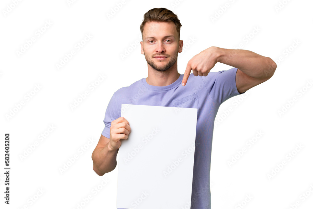 Young blonde caucasian man over isolated background holding an empty placard with happy expression and pointing it