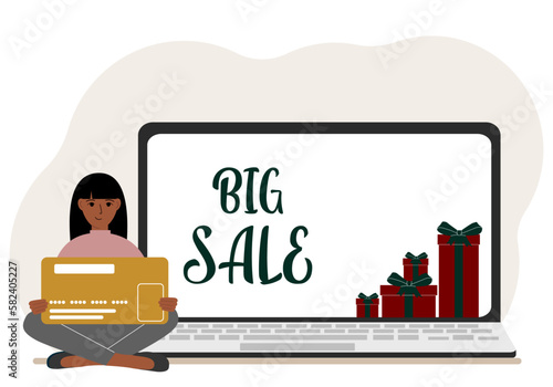 Online shopping. Big sale. A woman sits cross-legged in his hands holding a shopping card. Next to a laptop with gifts.