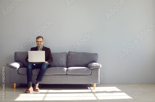 Mature businessman sitting on sofa working with laptop. Executive middle aged casually dressed man working in office lounge. Successful man working online via computer