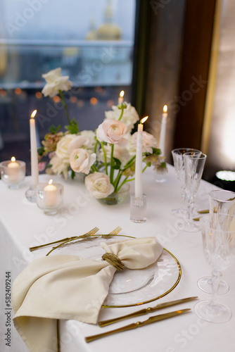Banquet table decorated with plates, cutlery, candles, glasses and flower arrangements