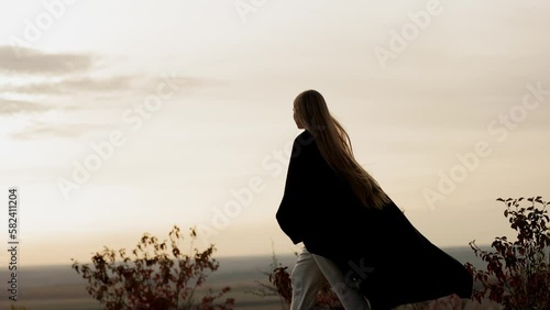 Young pretty long-haired woman girl walking alone on the edge of the mountain with an incredible view dressed in plaid, watching a beautiful sunset in the autumn evening