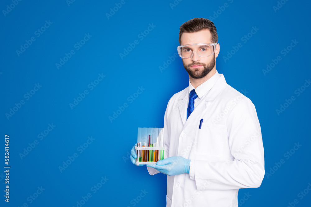 Portrait with copy space, empty place of attractive stylish scientist with bristle in white lab coat, tie holding test tubes with multi-colored liquid, looking at camera over grey background Portrait with copy space, empty place of attractive stylish scientist with bristle in white lab coat, tie holding test tubes with multi-colored liquid, looking at camera over grey background
