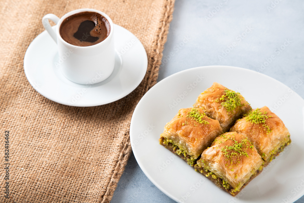 Pistachio baklava on a white plate with Turkish coffee.A plate of traditional baklava on burlap sack Pistachio baklava on a white plate with Turkish coffee.A plate of traditional baklava on burlap sack