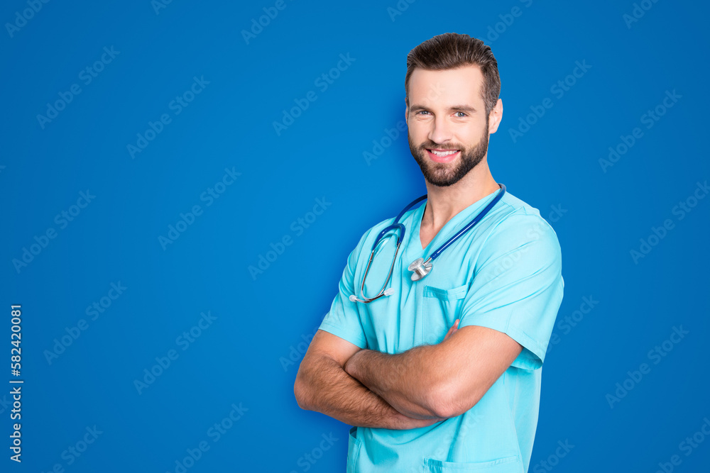 Portrait with copy space, empty place of positive cheerful man with stethoscope on his neck in blue lab uniform, having his arms crossed, isolated on grey background Portrait with copy space, empty place of positive cheerful man with stethoscope on his neck in blue lab uniform, having his arms crossed, isolated on grey background