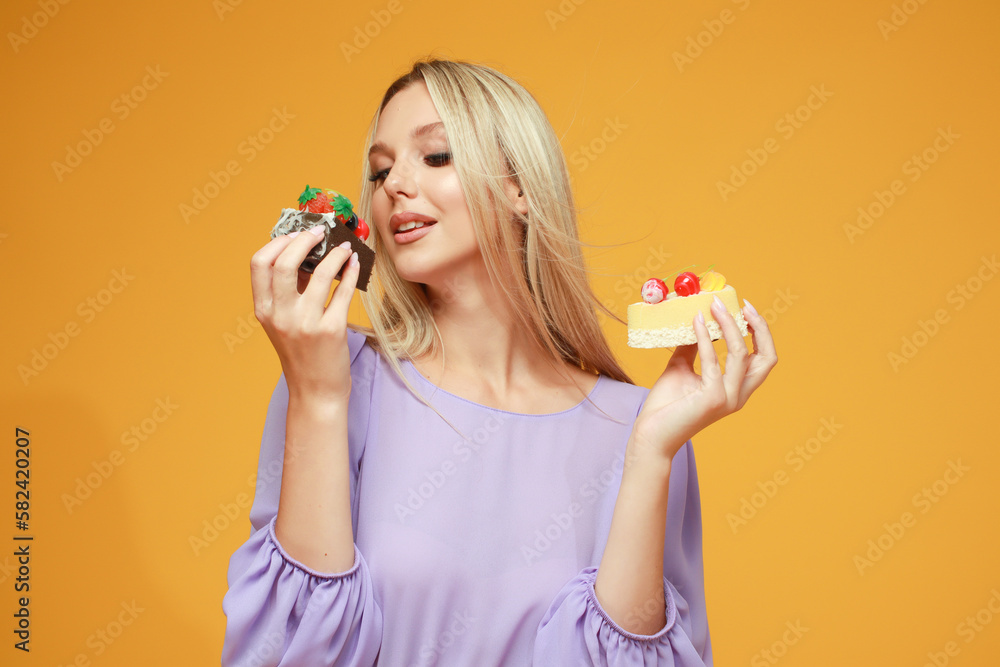 Beautiful blonde girl in a lilac dress with cakes on a yellow background. Studio. Diet and health Beautiful blonde girl in a lilac dress with cakes on a yellow background. Studio. Diet and health