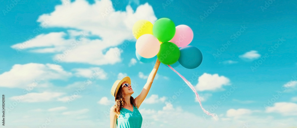 Happy smiling young woman with bunch of colorful balloons wearing summer straw hat on blue sky background Happy smiling young woman with bunch of colorful balloons wearing summer straw hat on blue sky background
