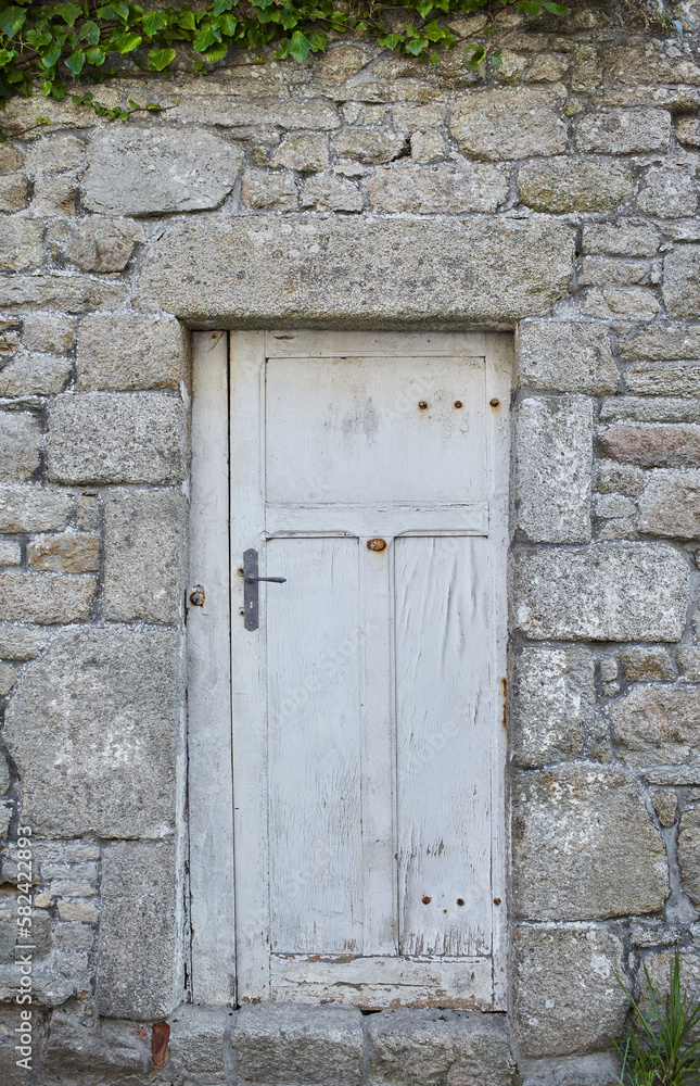 Port Louis, Bretagne, France : An old door with white paint that splits, embedded in an old grey stone wall