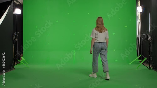 red-haired attractive white race young woman in jeans and a white T-shirt walks with her back to the camera on a green background. The girl turns around and gets scared