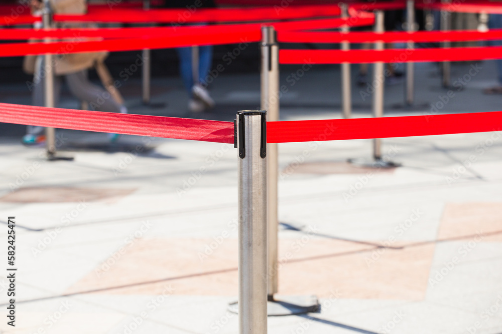 Red restrictive belts on metal posts for temporary fencing and control - organization of people movement Red restrictive belts on metal posts for temporary fencing and control - organization of people movement