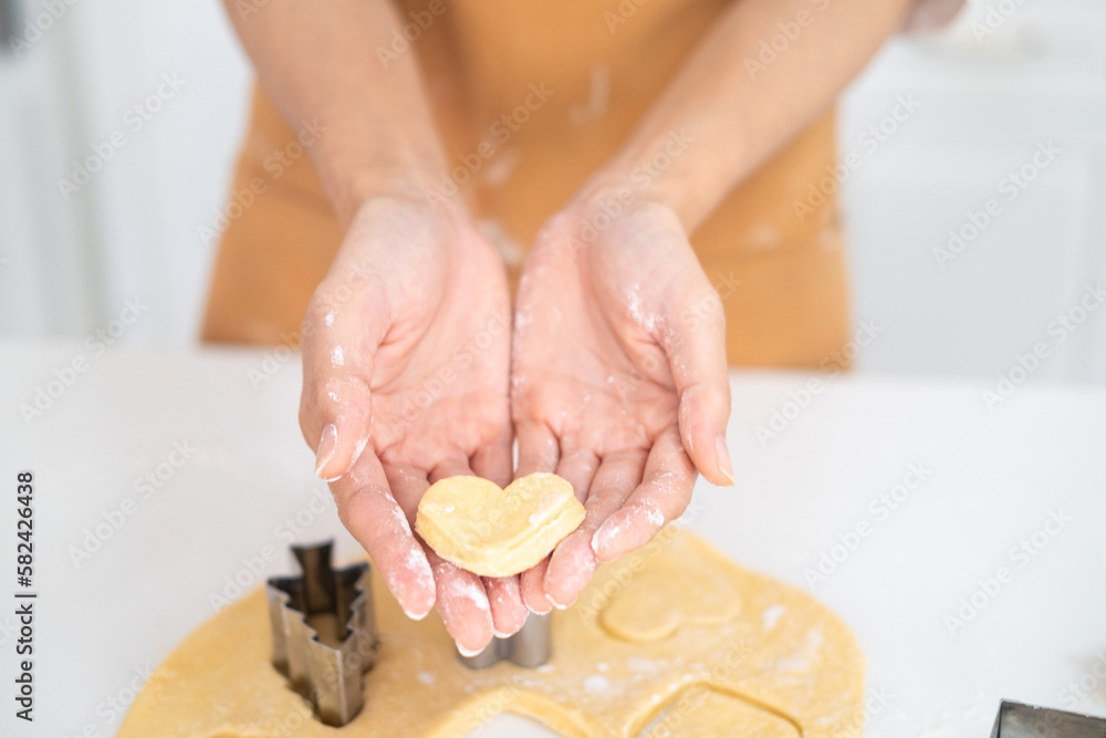 Cropped image of hands cutting cookies of dough while baking in kitchen .Making for homemade biscuits. On the table is dough and a set of cookie molds with other kitchen equipment.