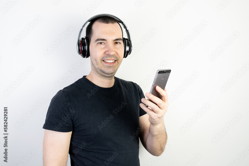 young man male guy model wearing headphones cool fashion style looks happy stand wear enjoy music good sound listening relax smile hold smartphone young man male guy model wearing headphones cool fashion style looks happy stand wear enjoy music good sound listening relax smile hold smartphone