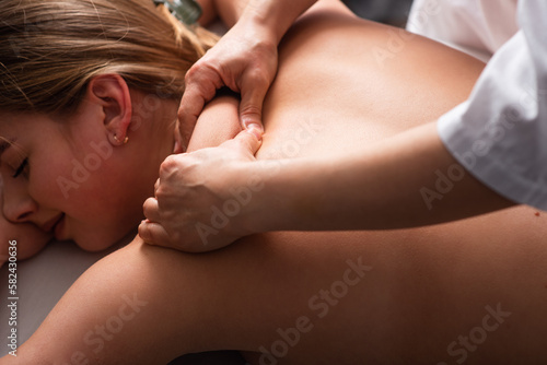 masseur massaging back and shoulder blades of young woman on massage table. Concept of massage spa treatments. Close-up