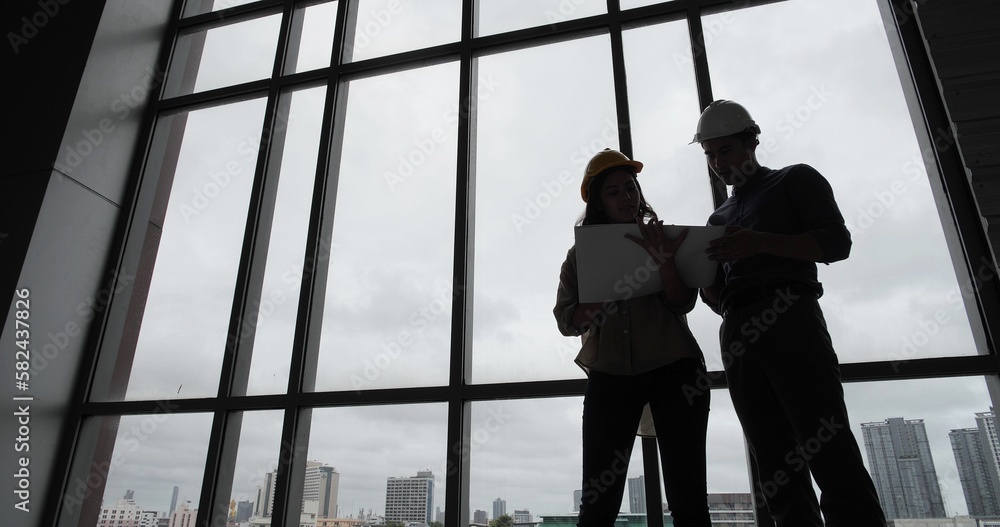 Two architect and engineer working on plans with blueprint standing near length window at cityscape with skyscrapers Two architect and engineer working on plans with blueprint standing near length window at cityscape with skyscrapers