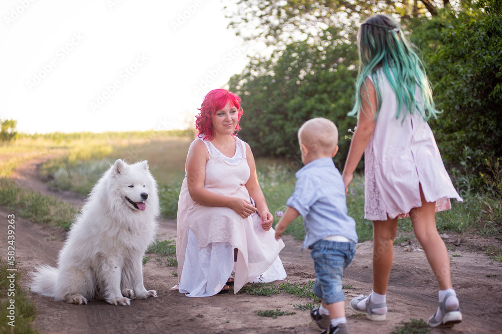 Girl with little boy carry gift of bouquets of wildflowers to mother with pink hair. Traveling with white Samoyed dog for walk. Diversity, creative family on the forest path. Summer trip on the field