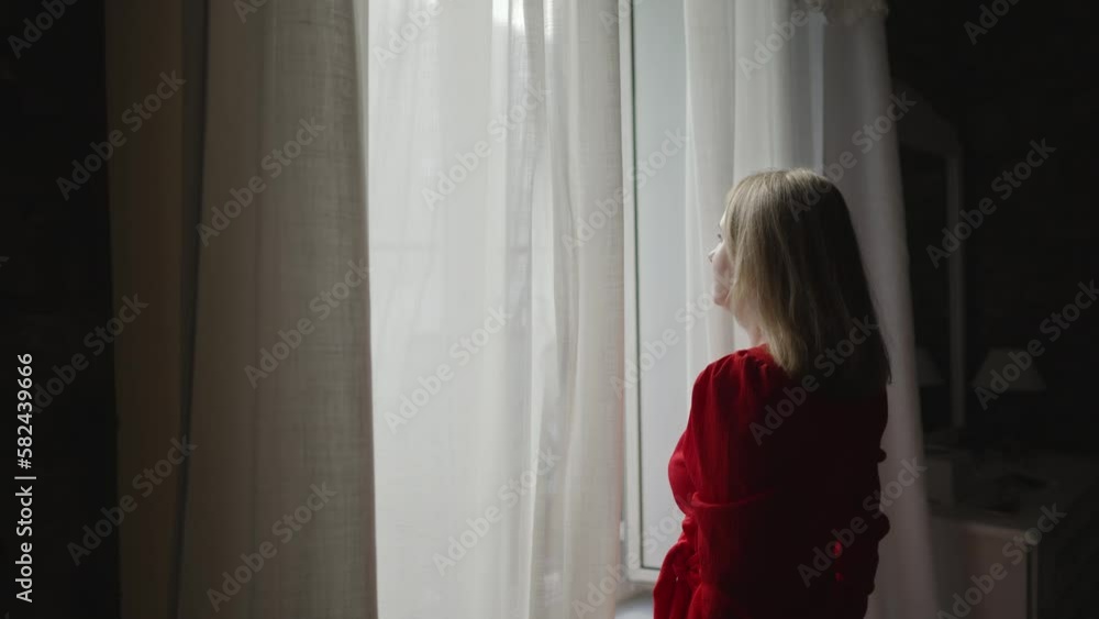 Woman opening curtains in her apartment. Woman opening curtains in her apartment.