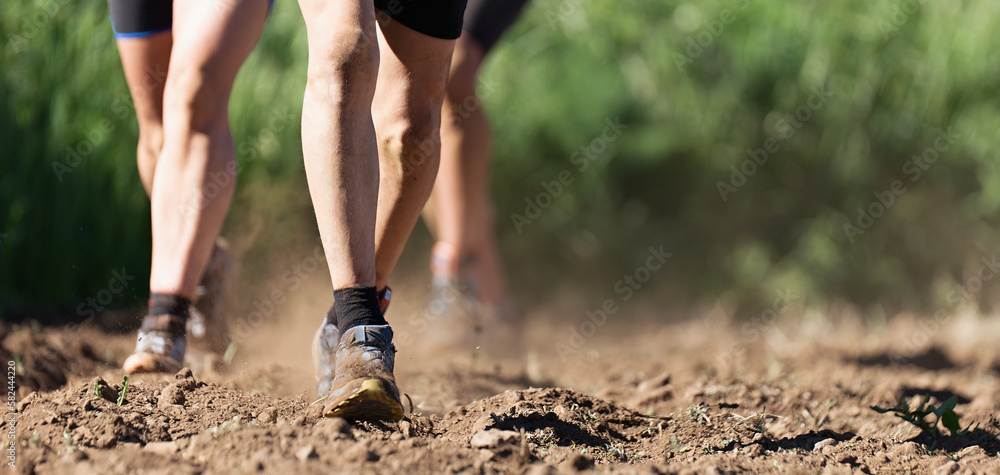 Trail running athletes exercising for fitness and health outdoors plowed field, closeup of running shoes in action Trail running athletes exercising for fitness and health outdoors plowed field, closeup of running shoes in action