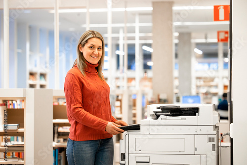 Fotografia Portrait of businesswoman standing by photocopier machine and copying or scanning documents inside large office